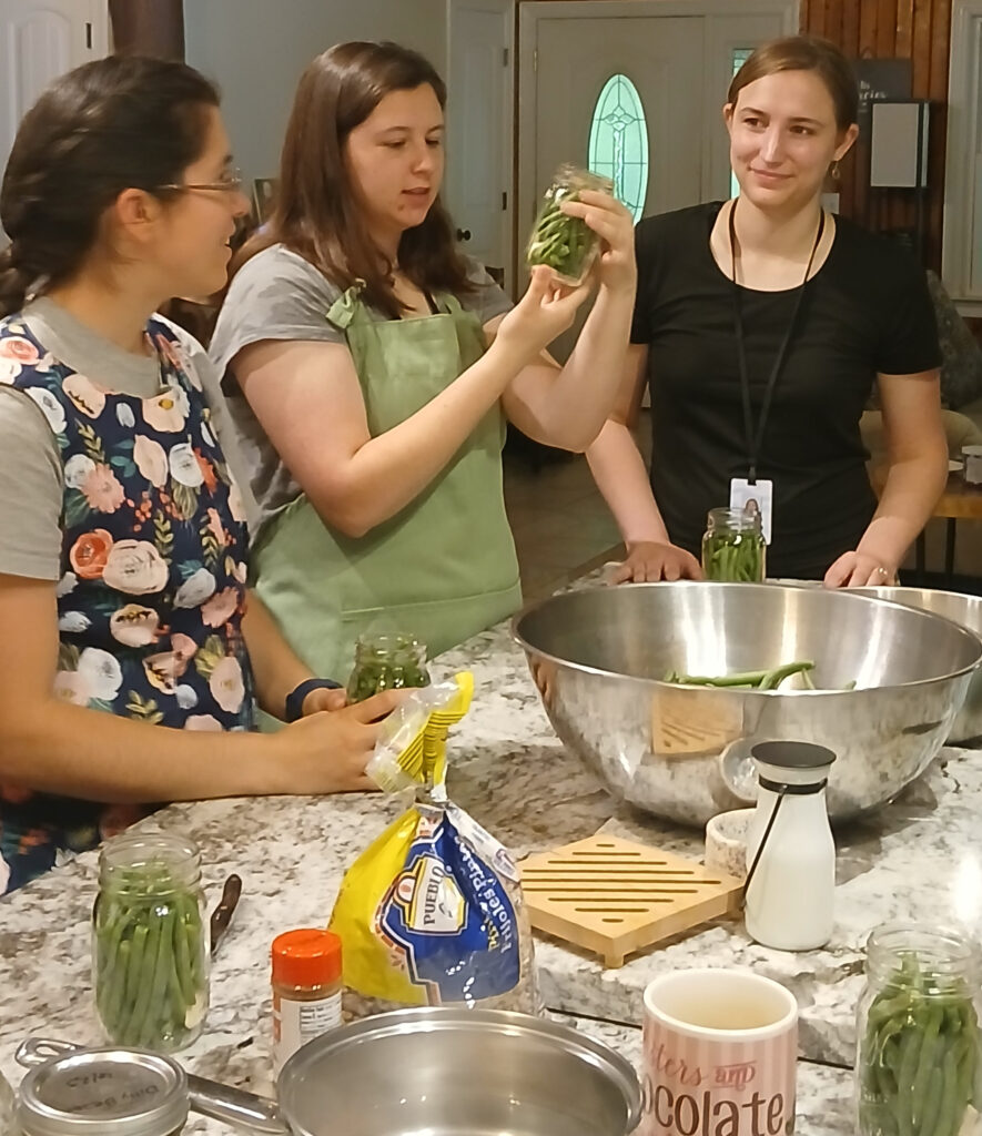 Three women pickle green beans at a kitchen counter