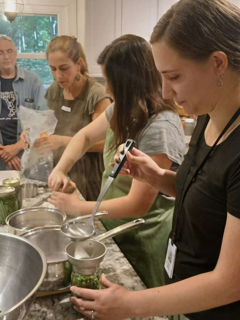 Three women pickle green beans at a kitchen counter.